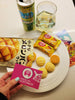 One of our Mascot Mix team members holds up Noginon's Snack Track card, above a plate of Melon Pan cookies and a couple of cheese cake flavored KitKat chocolates.